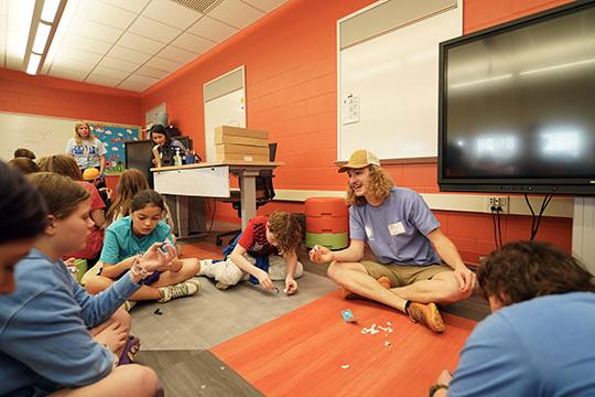 young man with long hair and hat talking to children